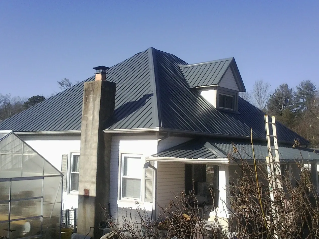 Dark blue standing seam metal roof on a white farmhouse with dormer — Slate & Tile Roof Repair by Roofing Brothers in Cave Springs