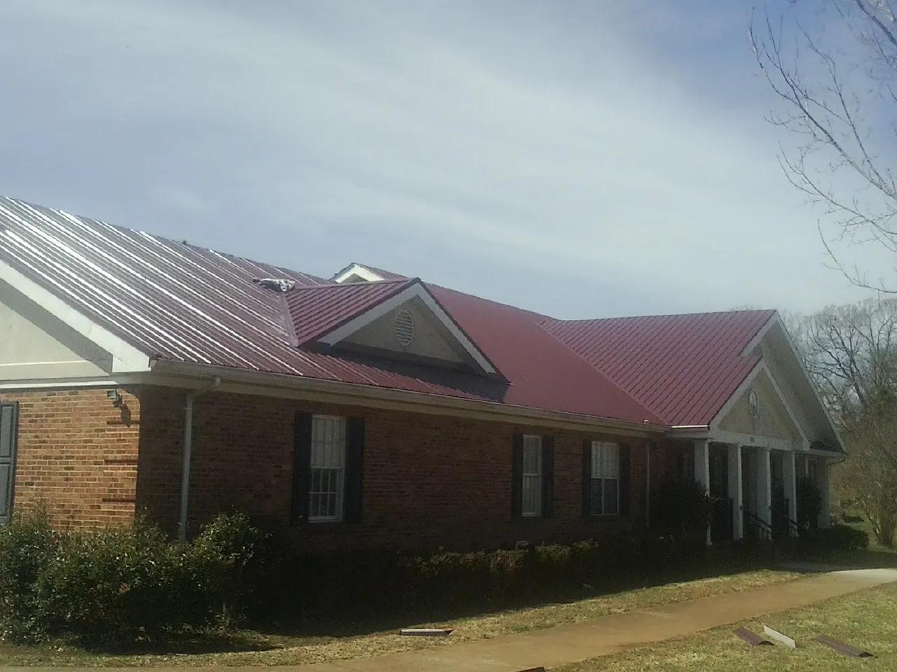 Red metal roof with gabled entries on a long brick building, from a Hail Damage Roof Repair job in Cave Springs