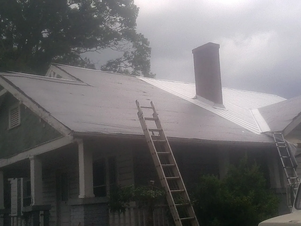 Ladders against a metal roof on an older home with a brick chimney in Cave Springs