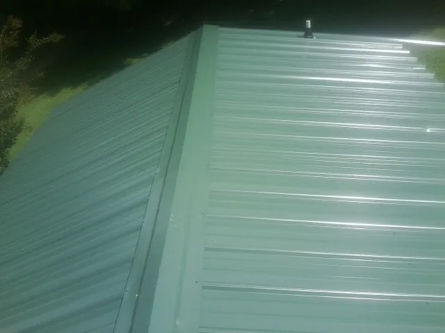New green metal panels meeting at the ridge of a roof — Flat Roof Repair work by our crew in Cave Springs