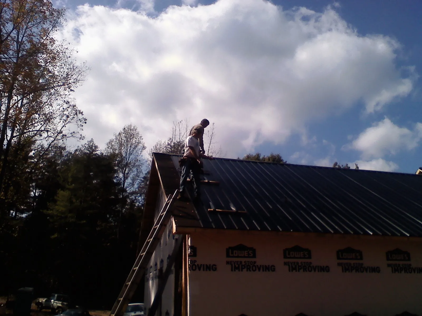 Roofer fastening dark metal panels high against a cloudy sky, from a Roof Inspection job in Cave Springs