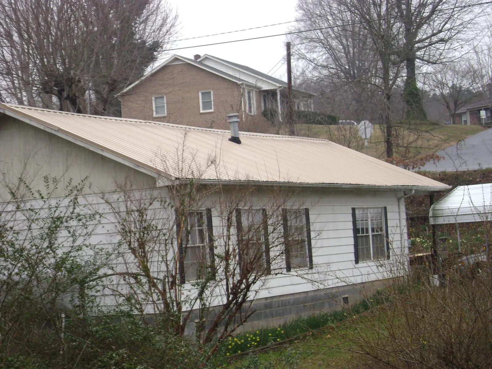 Tan metal roof on a white sided house set into a hillside — Commercial Roofing by Roofing Brothers in Cave Springs