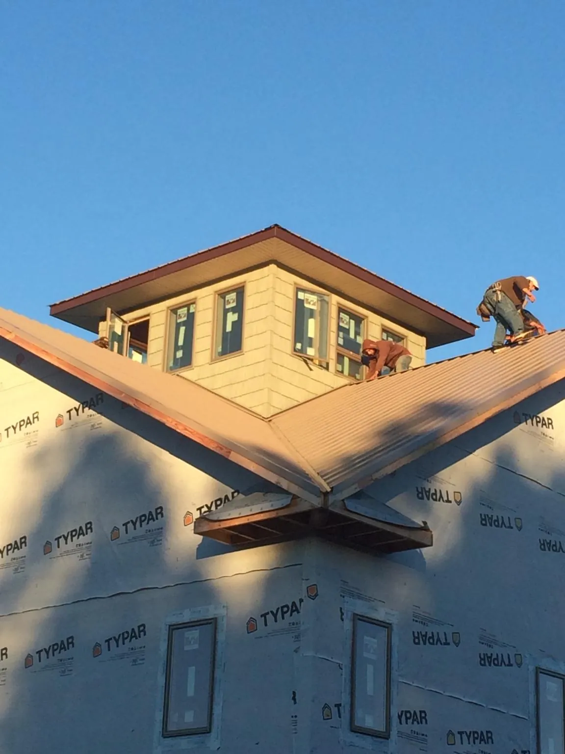 Roofers working around a rooftop cupola on a new metal roof at sunset — Roof Waterproofing in Cave Springs by Roofing Brothers